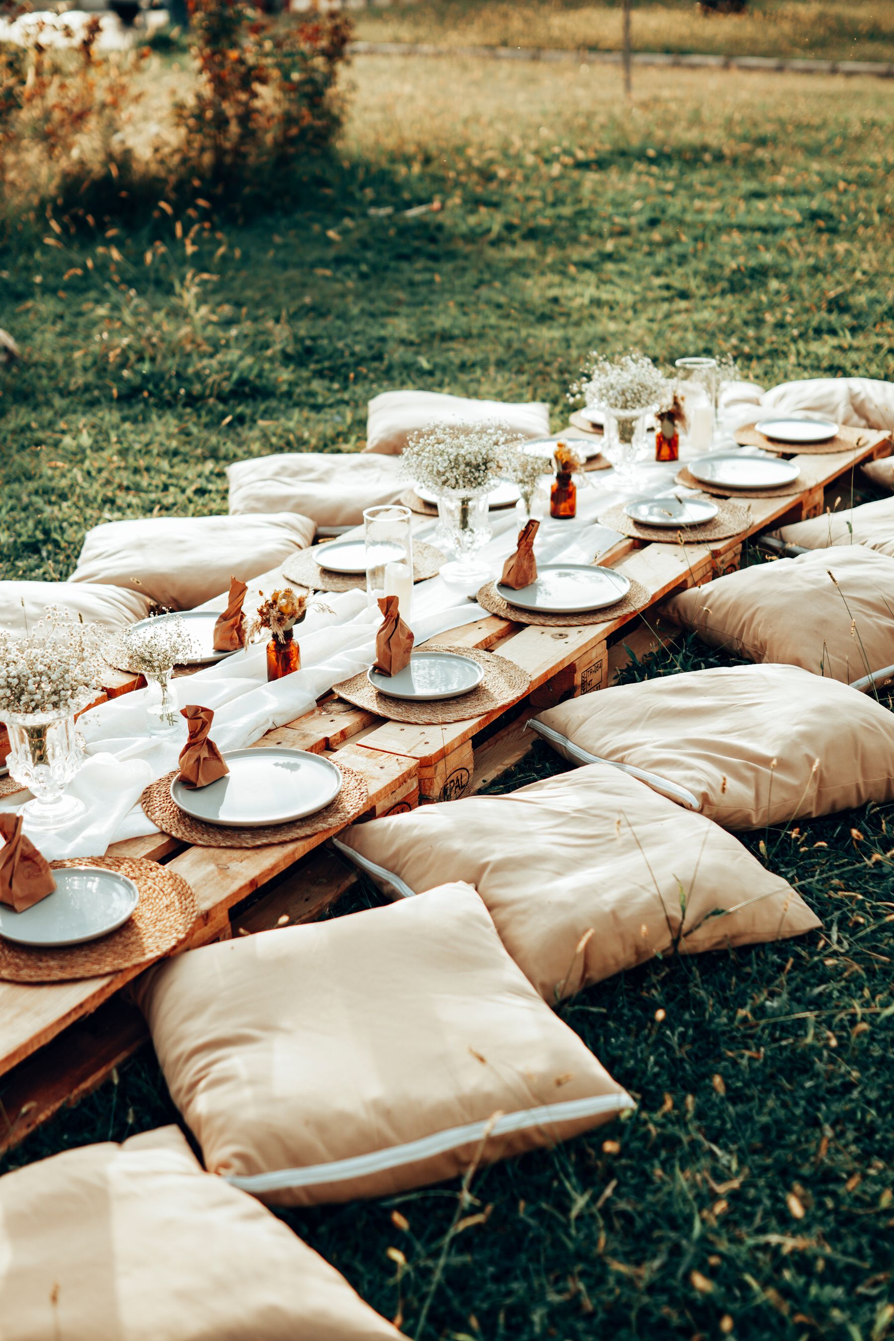 Illustrative stock photograph of an outdoor picnic with low tables, neutral cushions, and curated tableware