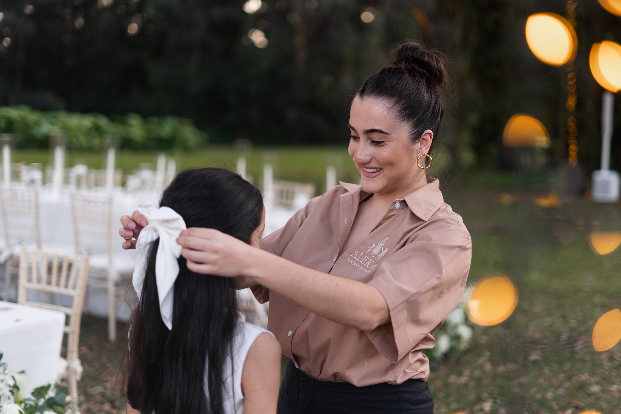 Professional nanny adjusting flower crown for children at elegant outdoor wedding ceremony with white flowers